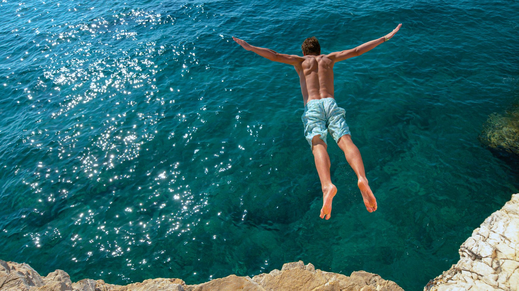 man cliff jumping into ocean