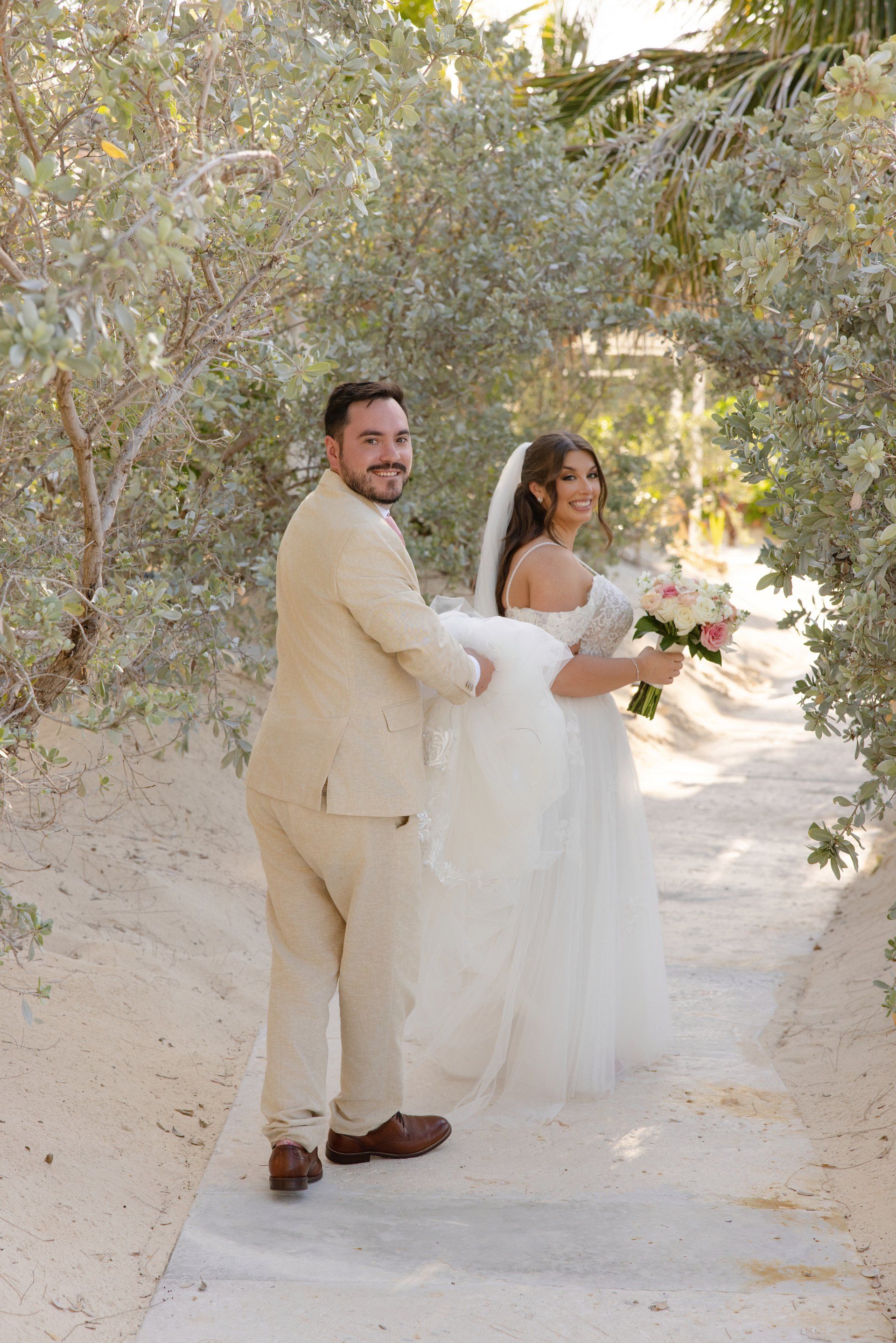 Bride walking down a sandy path surrounded by greenery on her wedding day