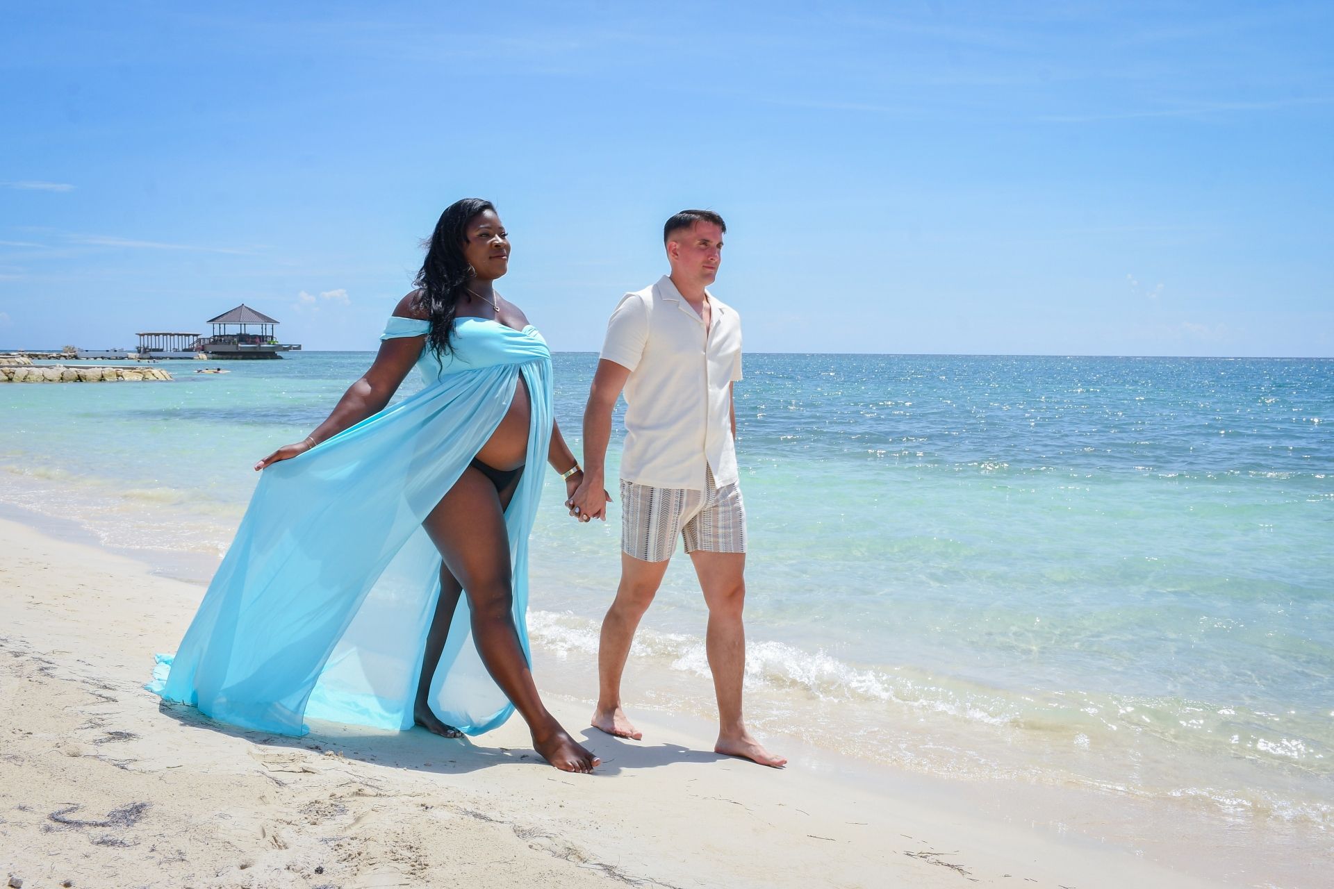 Pregnant couple walking along the beach during their Sandals babymoon in Jamaica