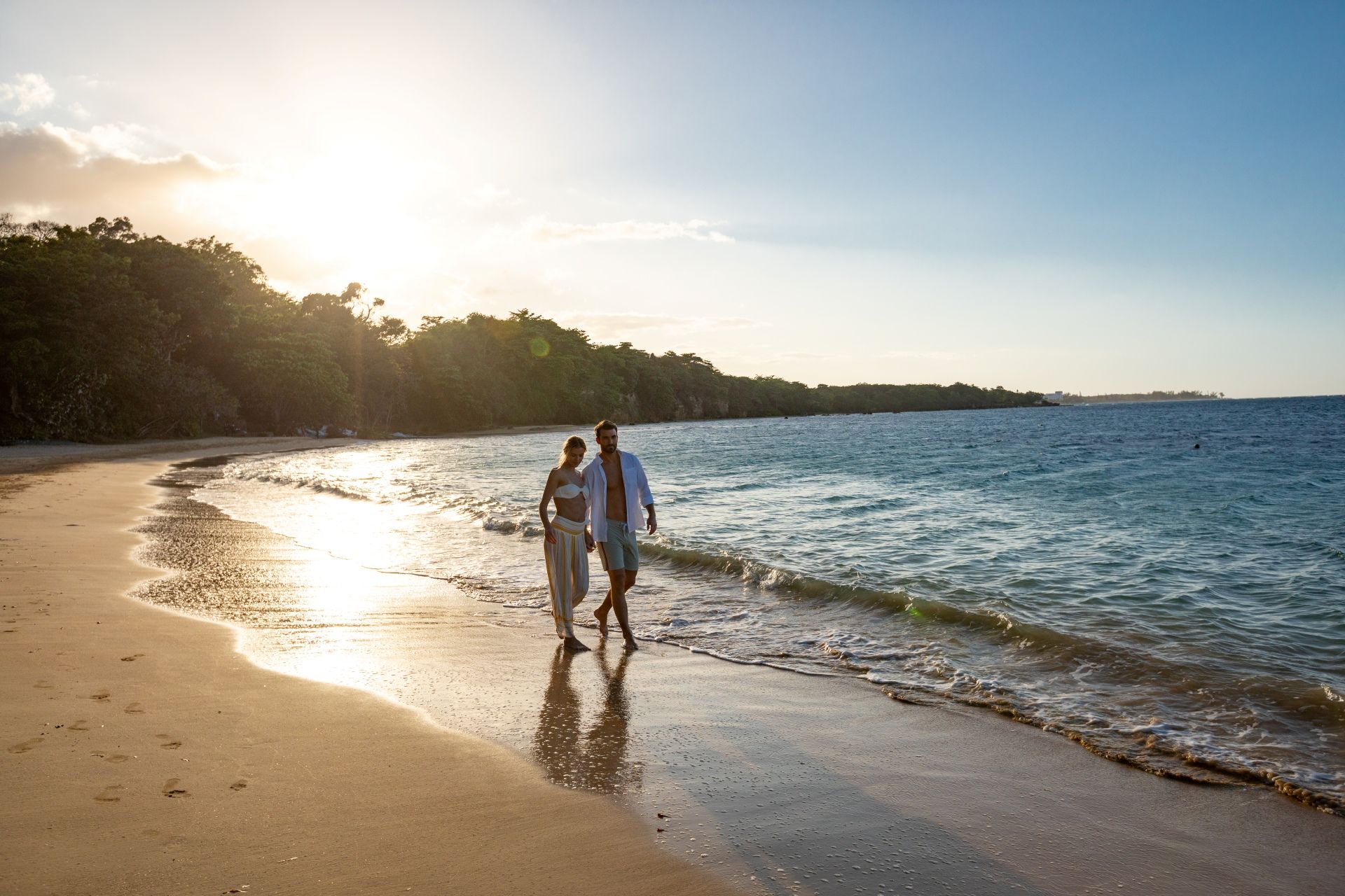 Couple walking along Caribbean beach at sunset after romantic proposal